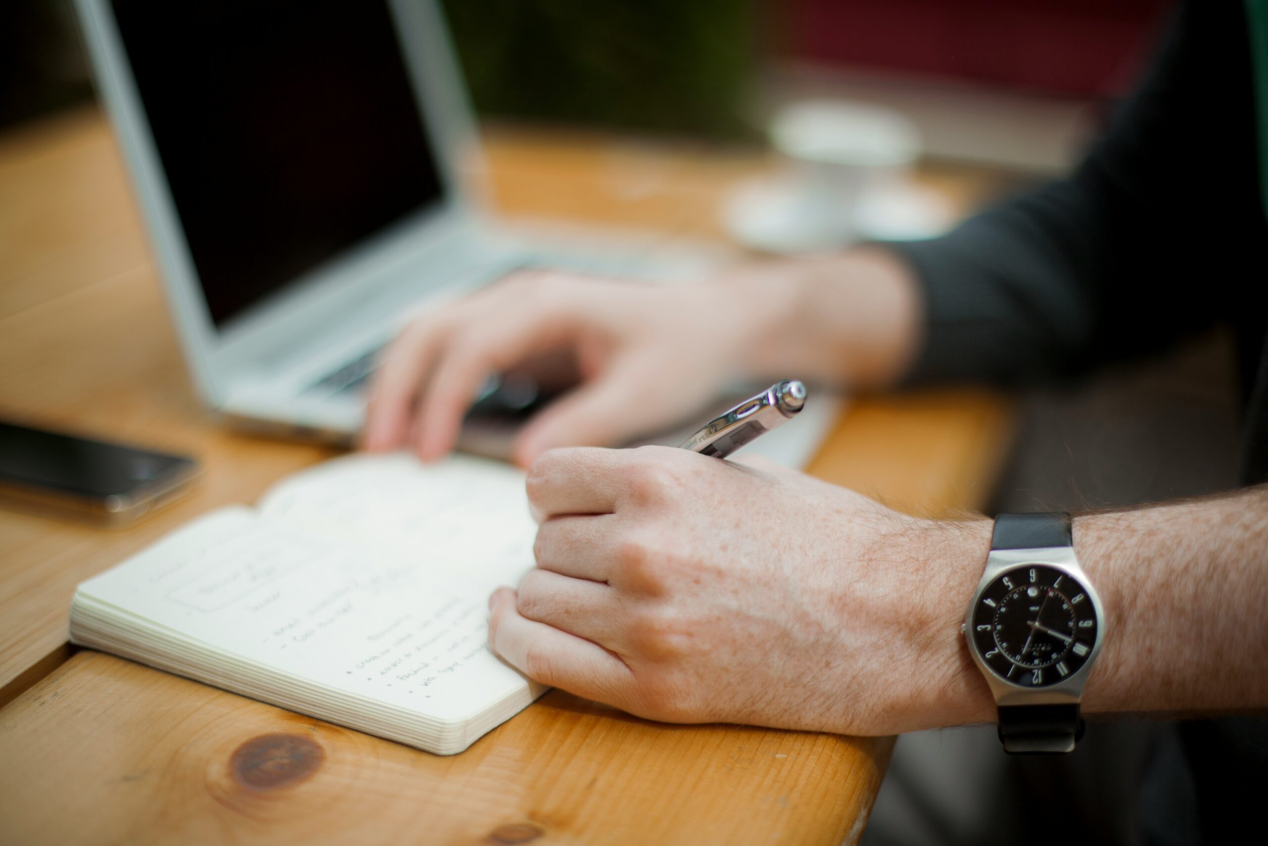 A person writing in a notebook next to a laptop, emphasizing the need for strategic content planning and organization to take action and select the best CMS for your small business.