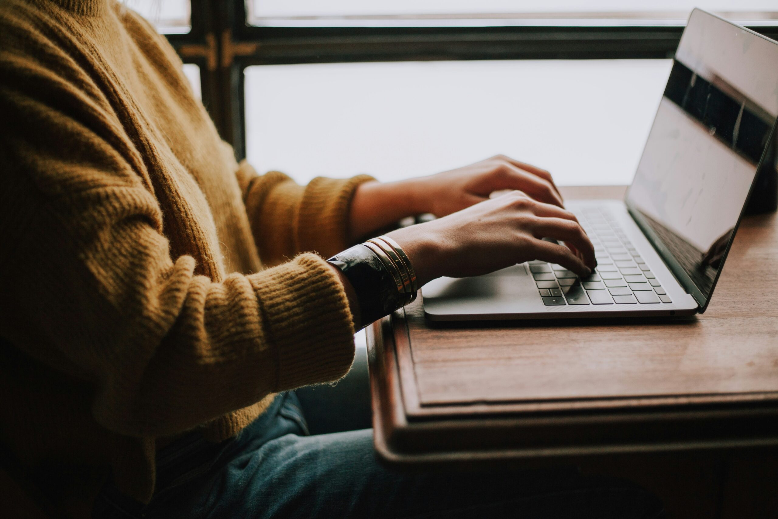 Hands typing on a laptop with a warm-toned sweater, representing a user working on a content management system interface.