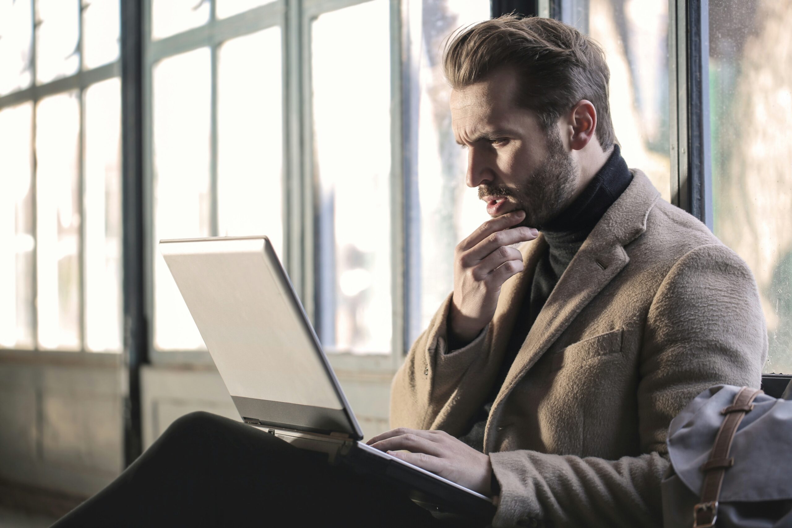 A man looking thoughtfully at his laptop, illustrating the decision-making process when choosing between a Headless CMS and a traditional CMS.