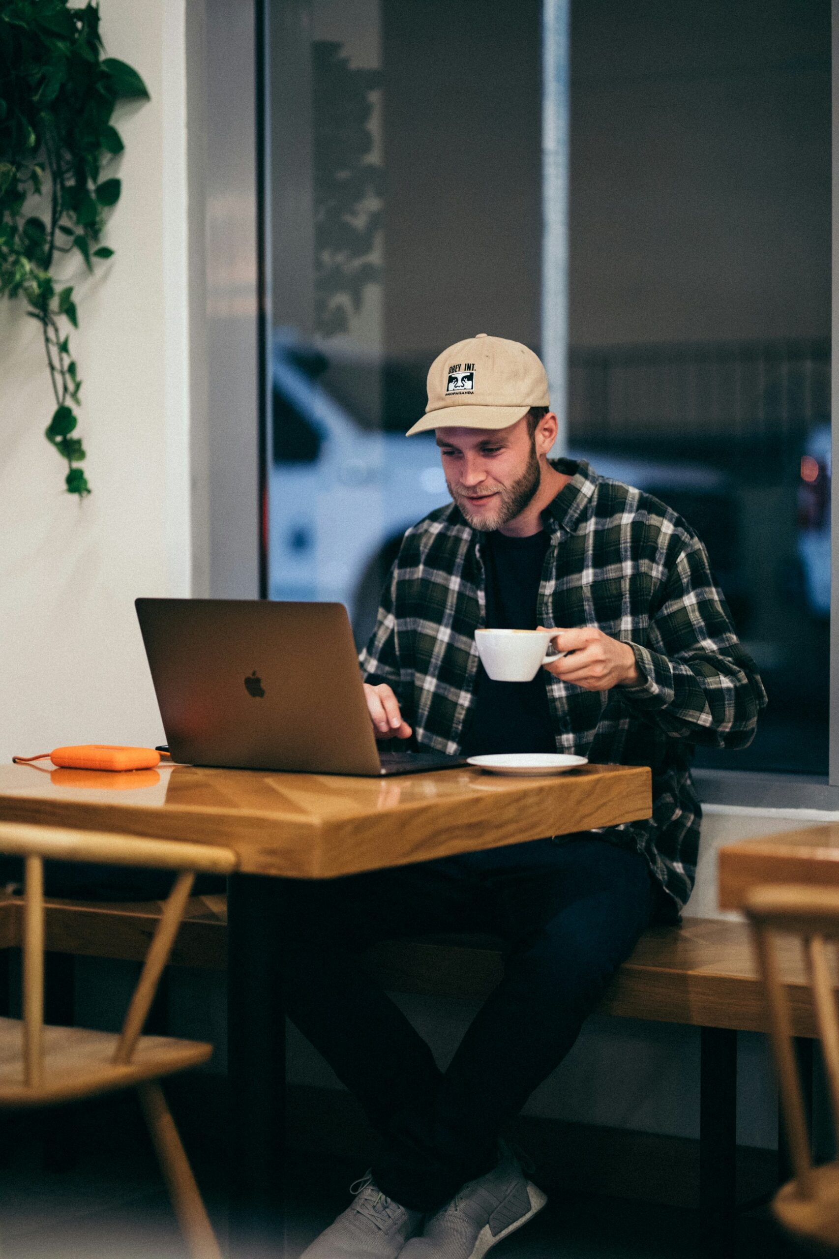 A man in a café using a laptop, illustrating the accessibility and ease of use of proprietary CMS solutions for businesses, compared to the greater customization and control offered by open-source CMS.