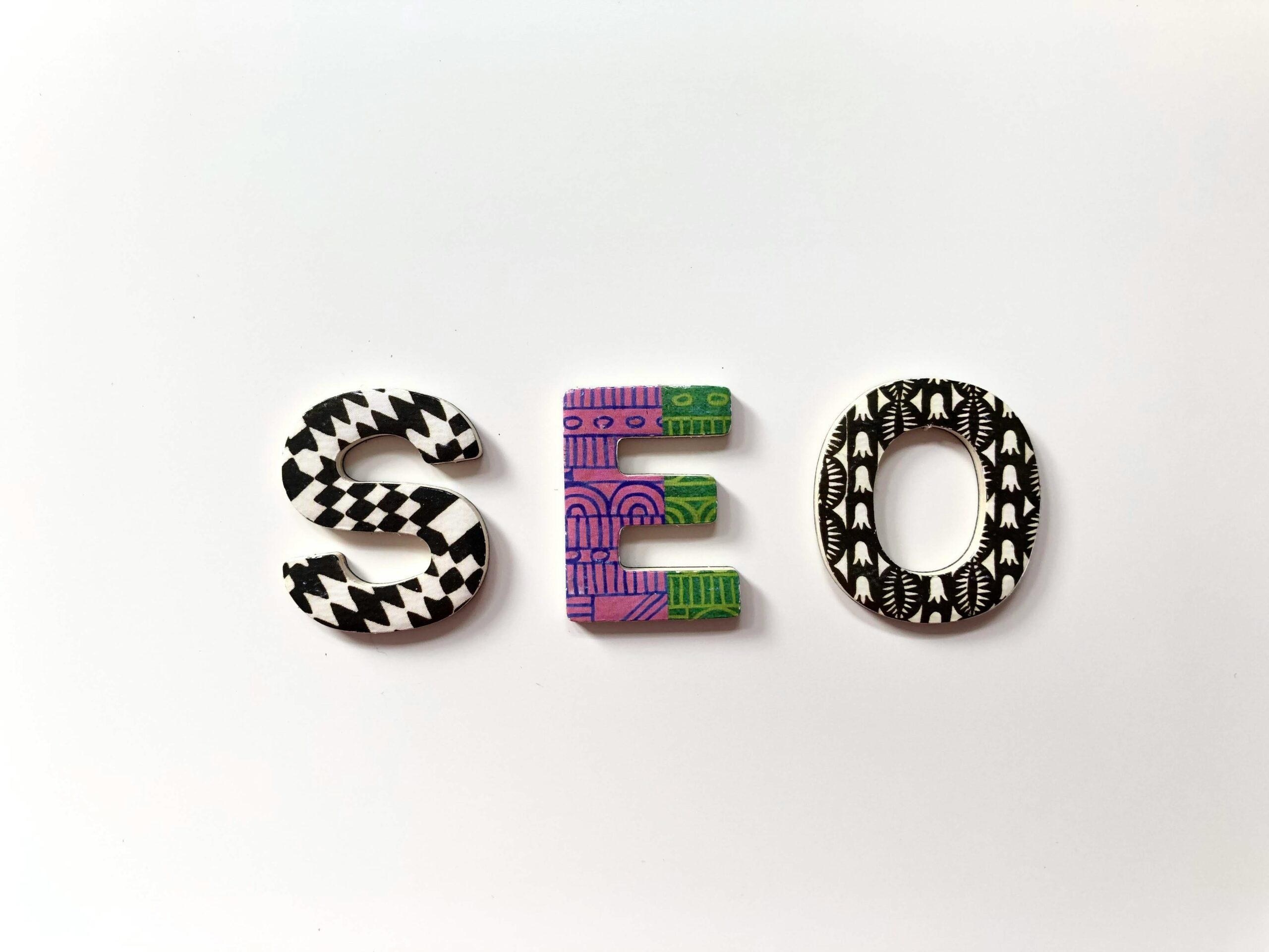 The word 'SEO' in decorative letters, showcasing the built-in SEO features of CMS compared to traditional web development.