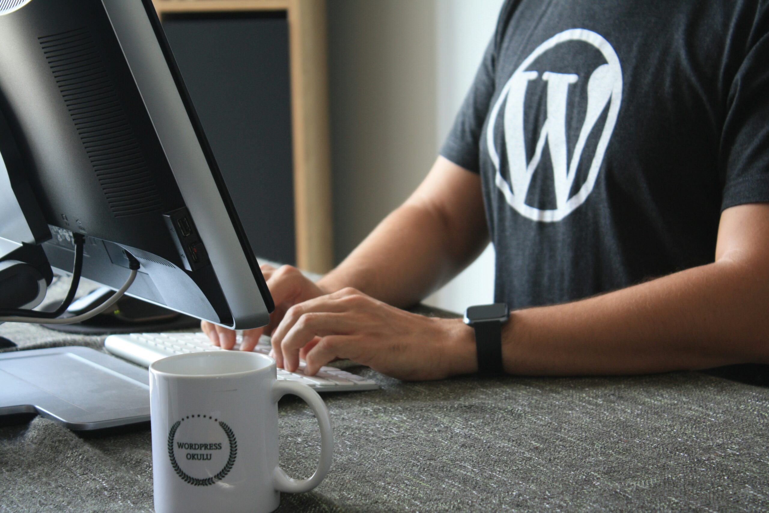 A person wearing a WordPress t-shirt typing on a computer, showcasing WordPress as a popular CMS choice for small enterprises.