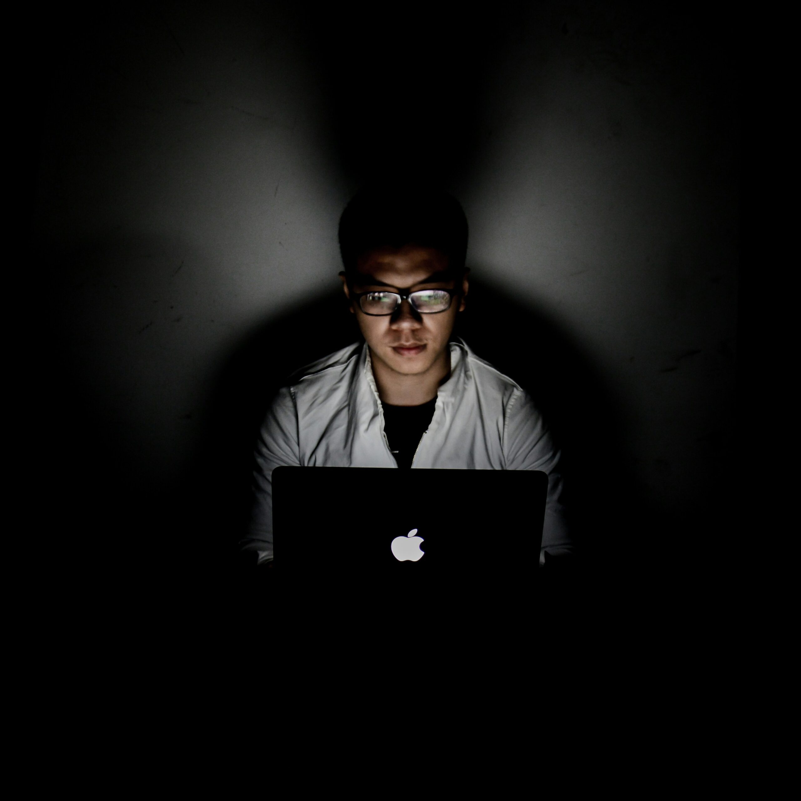 A focused individual wearing glasses and a white jacket working on a laptop in a dimly lit room, symbolizing the in-depth evaluation of popular front-end technologies.