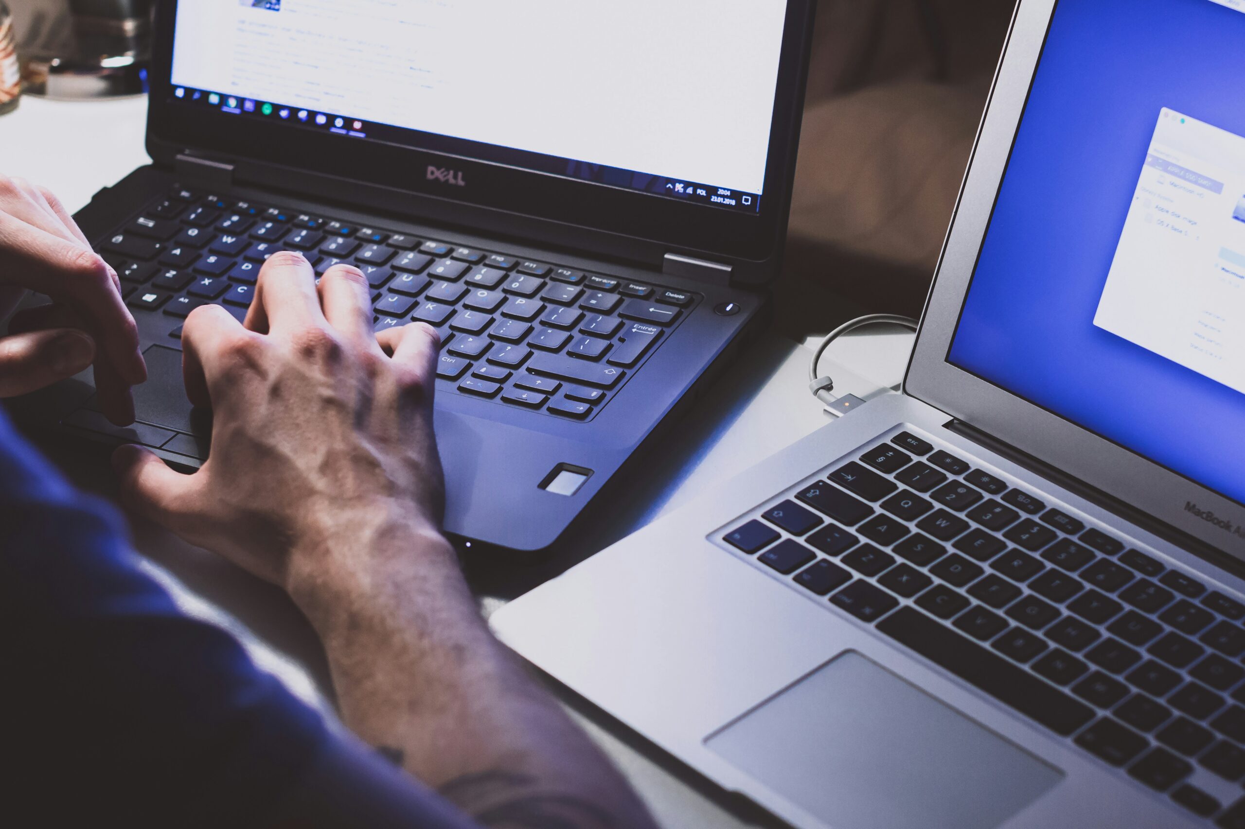 A person working on a Dell laptop with a MacBook beside it, representing the use of multiple tools and techniques for optimizing front-end performance.