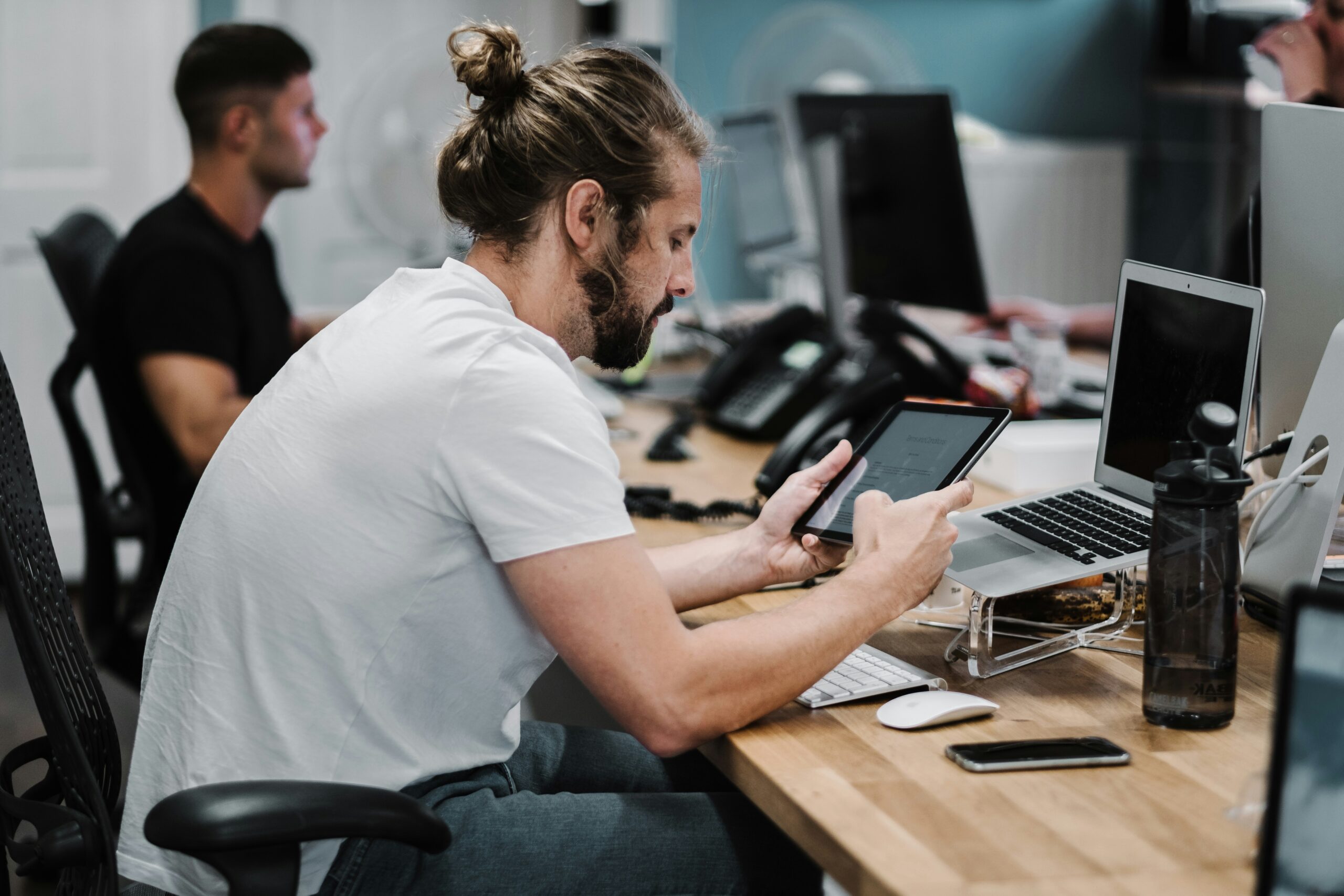 A focused professional in a modern office, reviewing technical details on a tablet while working on multiple devices, emphasizing the process of analyzing technical proficiencies.