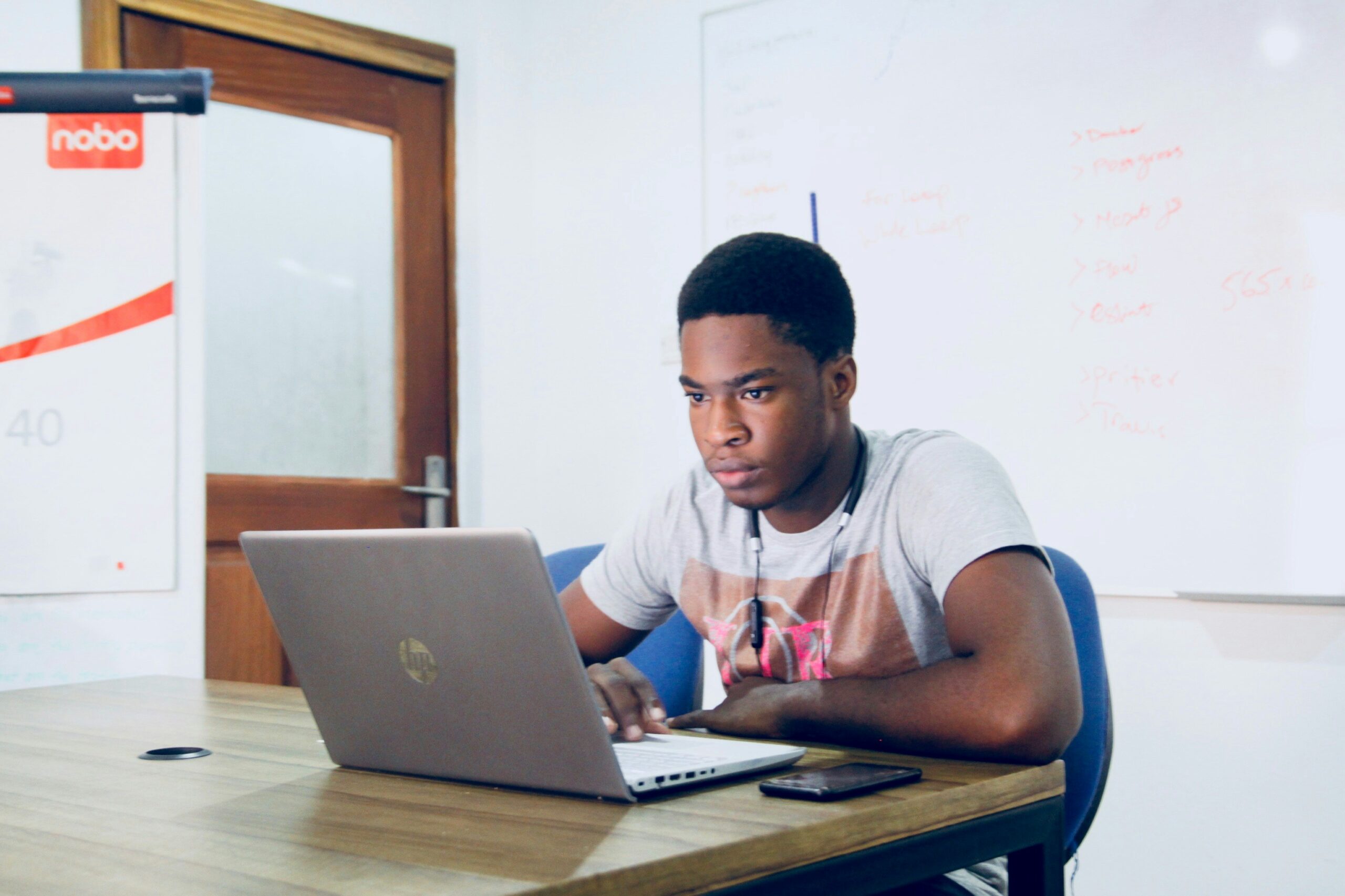 A focused developer working on a laptop in a meeting room with a whiteboard, analyzing and evaluating potential back-end development providers for project needs.