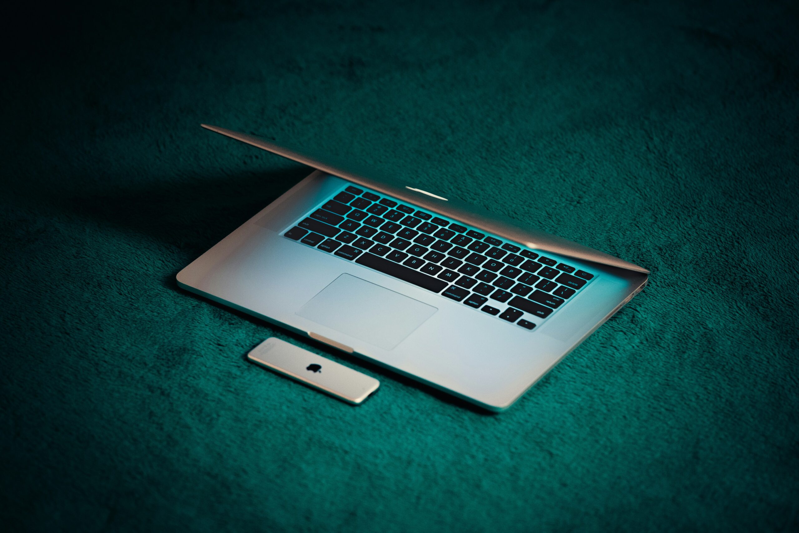 A sleek laptop with a partially closed lid and a smartphone placed beside it on a dark teal surface, symbolizing the exploration of front-end technologies.