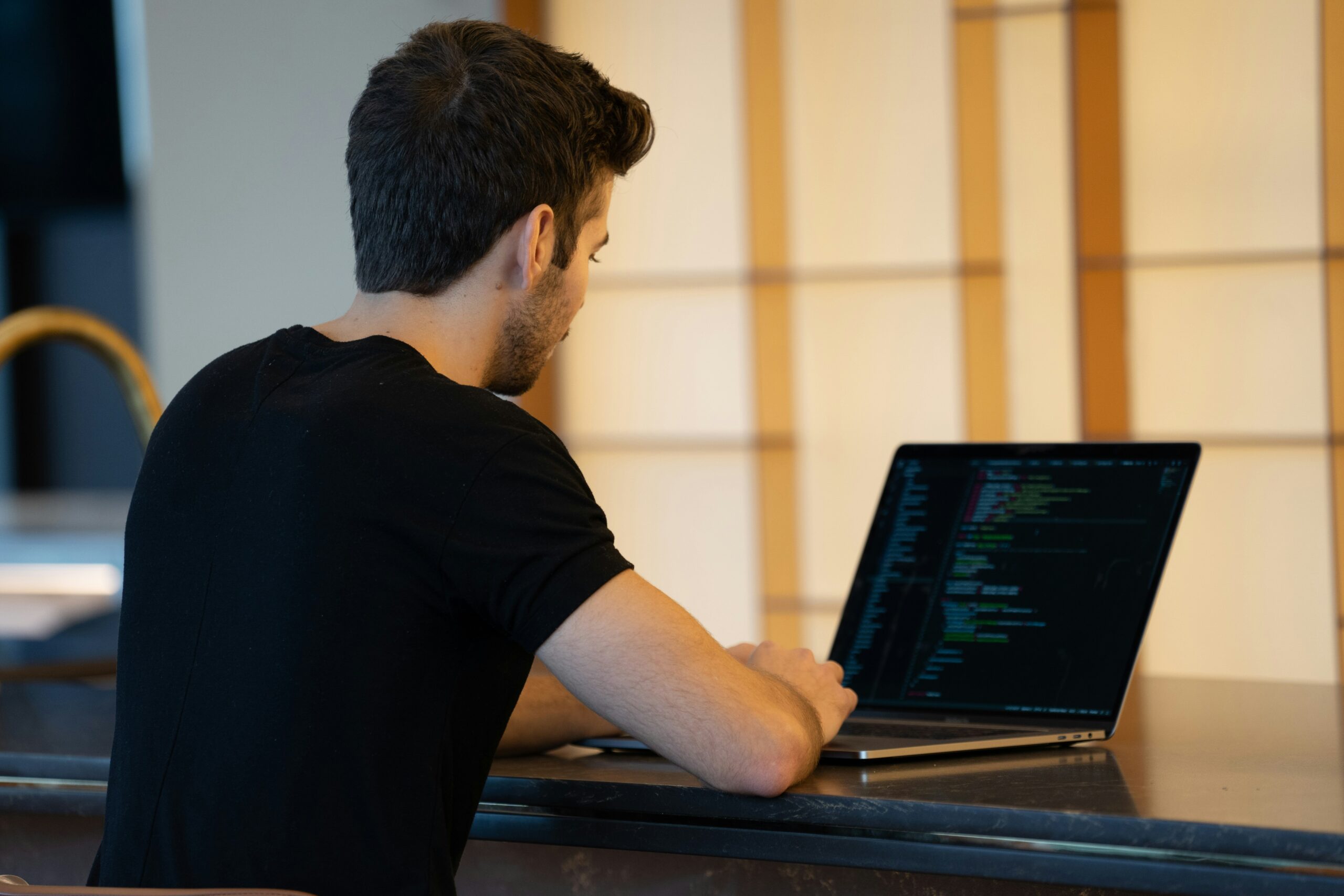 A developer in a black t-shirt working on a laptop with code displayed on the screen, highlighting the scalability and flexibility of custom solutions.