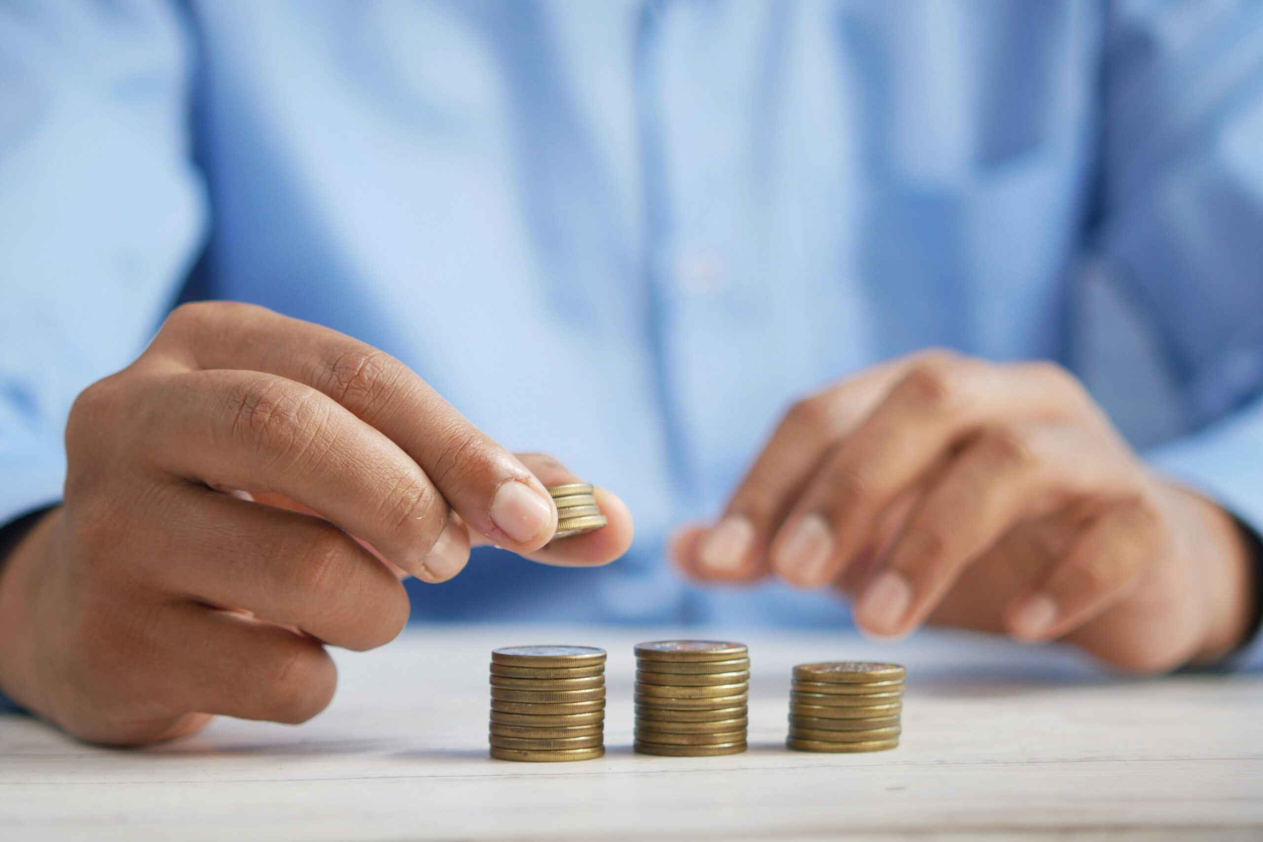 A person in a blue shirt stacking coins in ascending order, representing the cost implications of custom solutions versus templates.