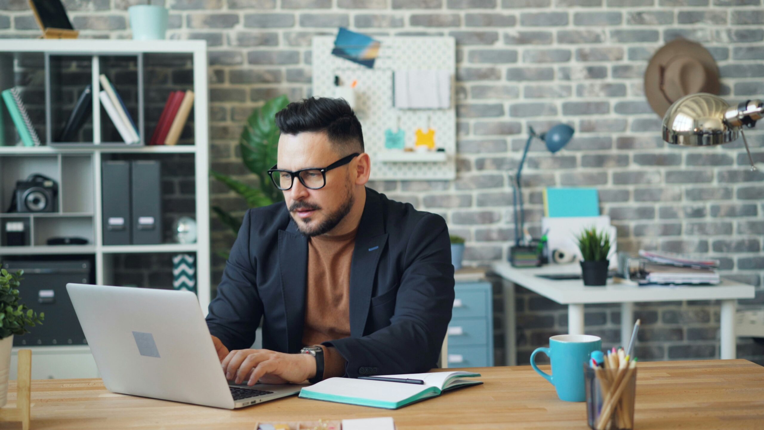 A man in a stylish office working on a laptop, researching back-end development services to enhance website functionality and performance.