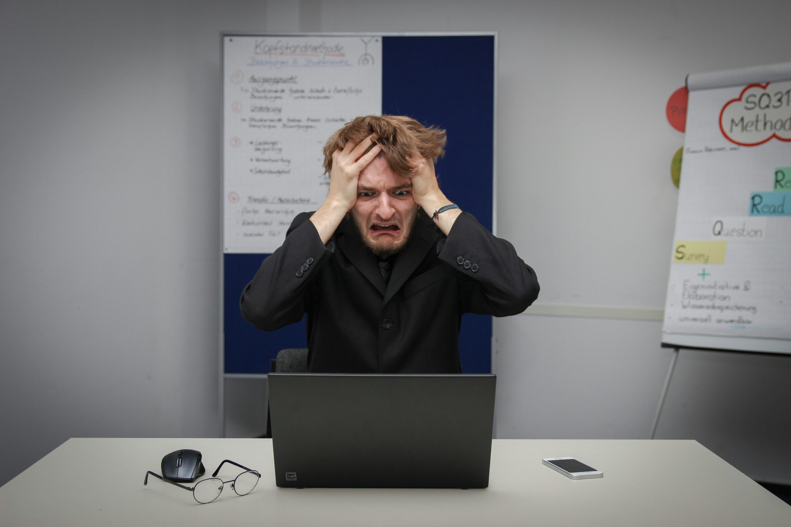 A frustrated man holding his head while looking at a laptop, representing the challenges faced in responsive web design and the process of overcoming them.