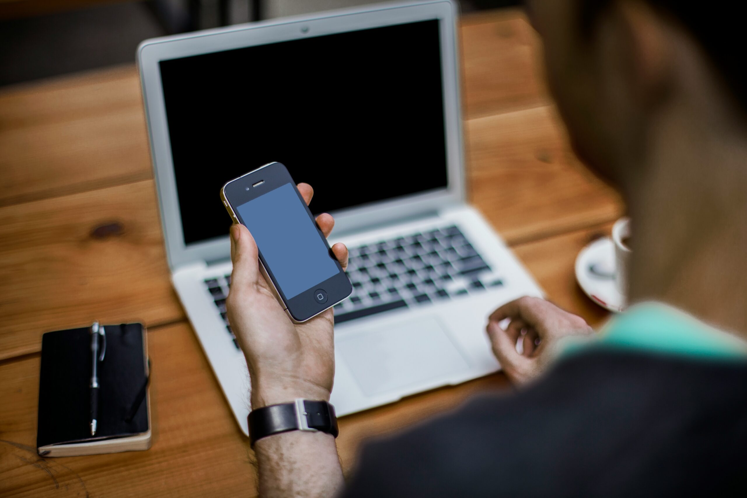 A person holding a smartphone in front of a laptop, representing the shift toward rethinking design structure by prioritizing a mobile-first approach. | Day by Day Digital A person holding a smartphone in front of a laptop, representing the shift toward rethinking design structure by prioritizing a mobile-first approach.