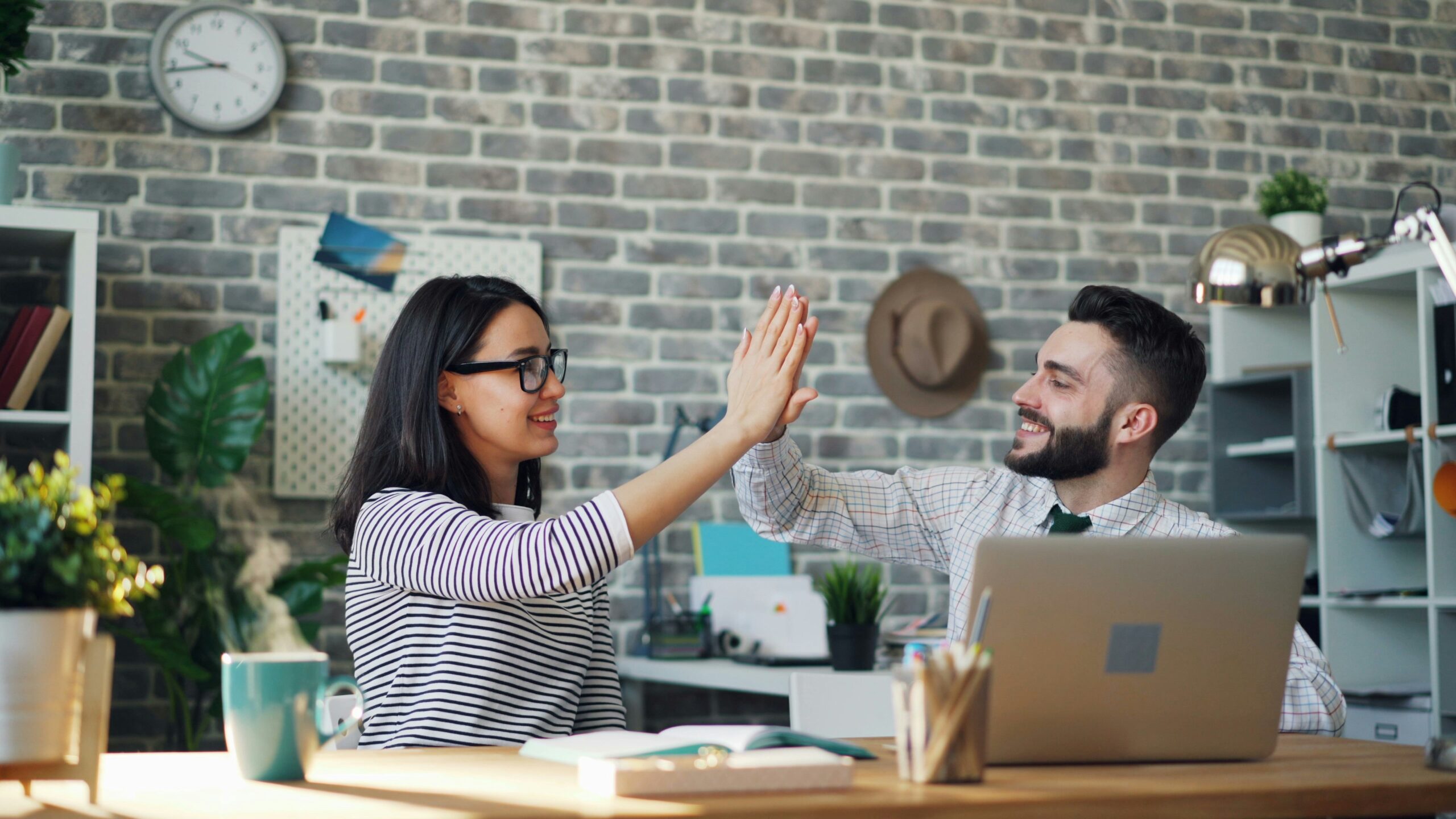 Two coworkers smiling and high-fiving at a desk, symbolizing the ease and speed of launching a project using pre-built templates that save time and money. | Day by Day Digital Two coworkers smiling and high-fiving at a desk, symbolizing the ease and speed of launching a project using pre-built templates that save time and money.