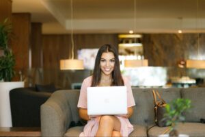 A smiling woman working on a laptop in a stylish lounge reflects the modern flexibility and range of pricing models available for SEO content writing services.