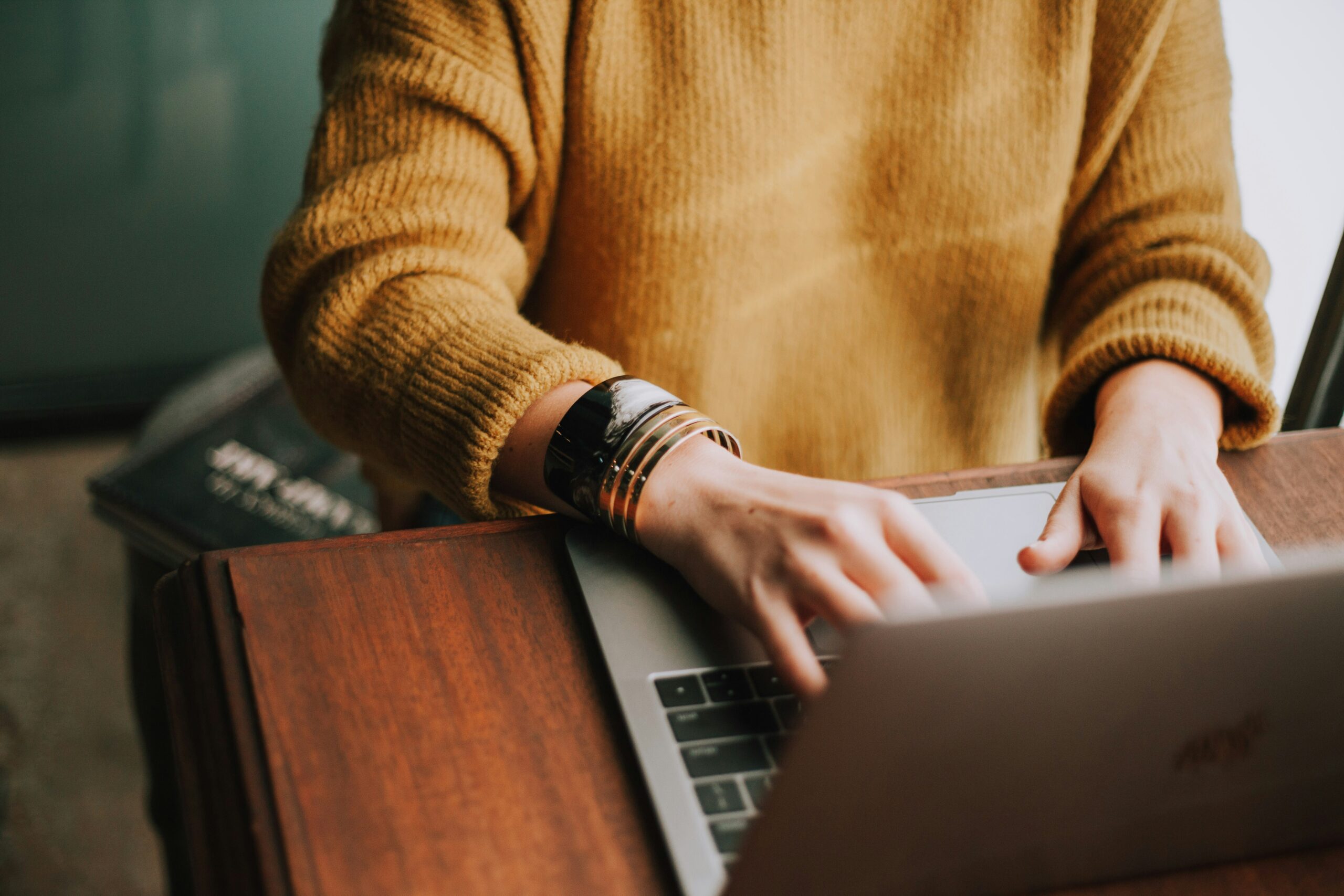Person in a mustard sweater typing on a laptop at a wooden desk, symbolizing focused e-commerce keyword research to improve online search rankings.