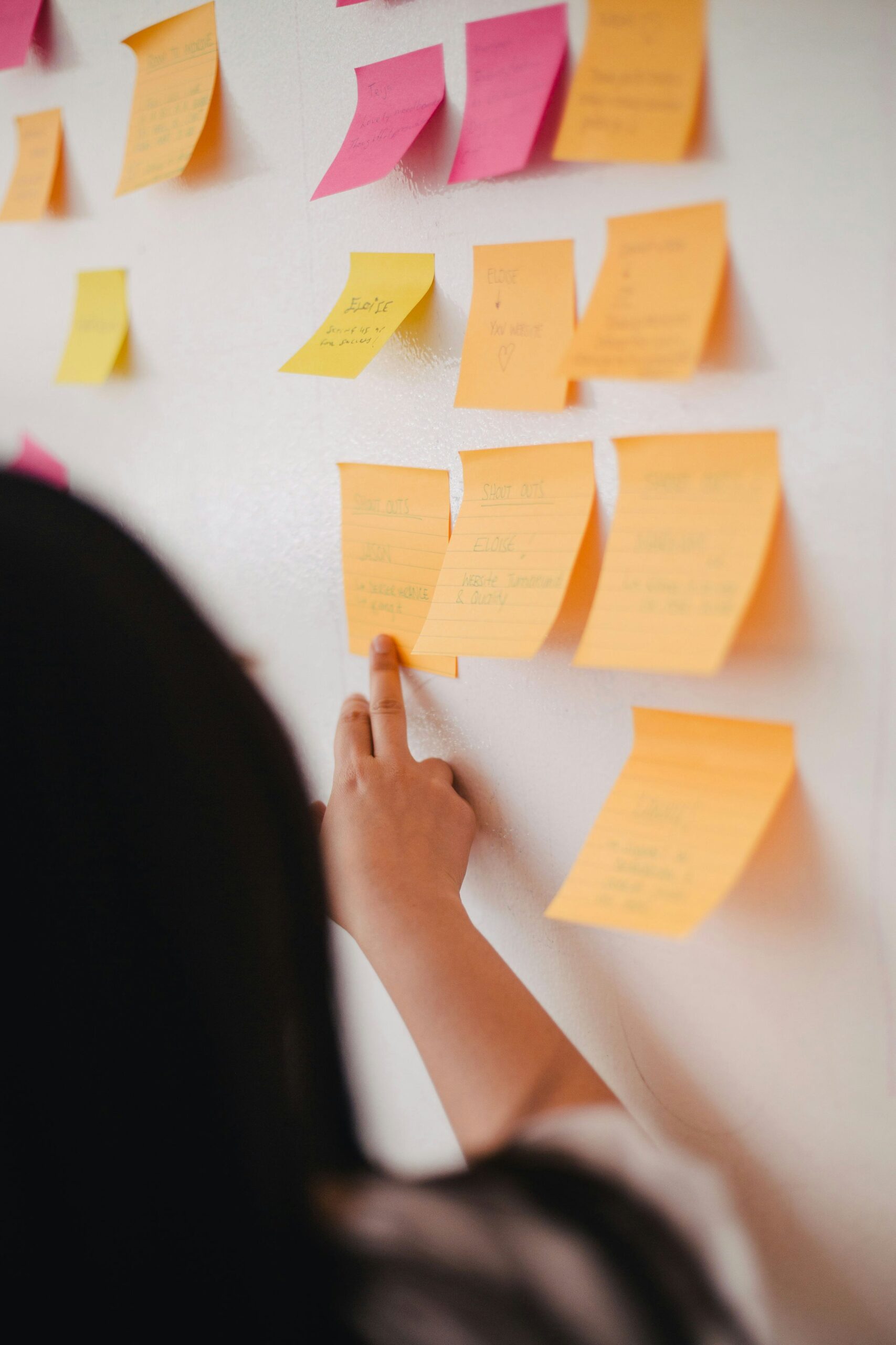 A person organizes colorful sticky notes on a wall, representing the planning and structure involved in creating a successful content promotion strategy. | Day by Day Digital A person organizes colorful sticky notes on a wall, representing the planning and structure involved in creating a successful content promotion strategy.