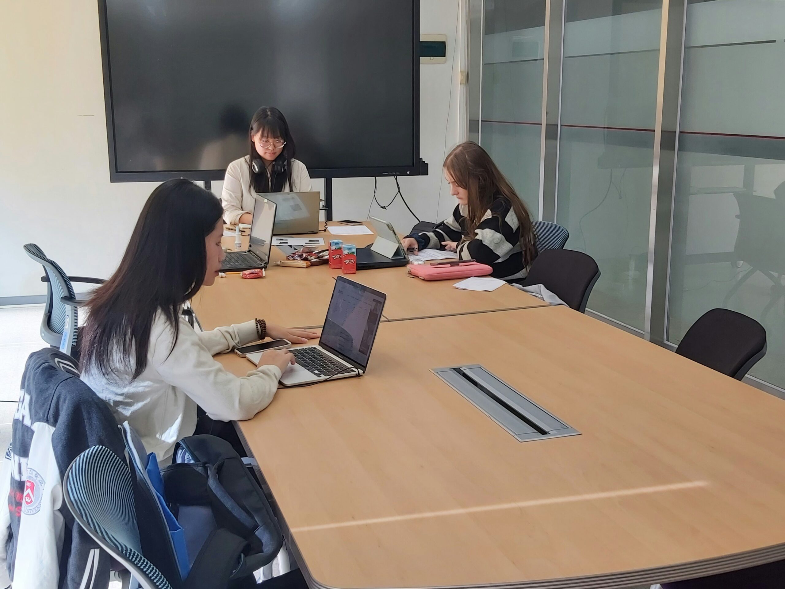 Three team members working on laptops in a modern meeting room, illustrating collaboration in streamlining an efficient SEO content workflow.