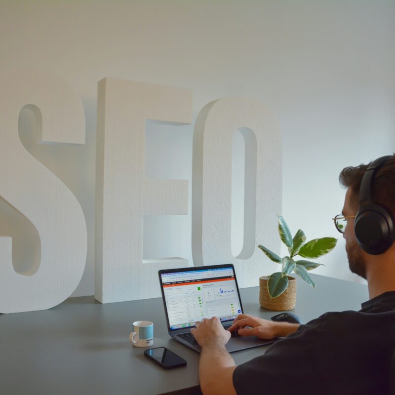 A digital marketer analyzing performance metrics on a laptop beside large SEO letters, representing the key elements behind successful SEO content marketing.