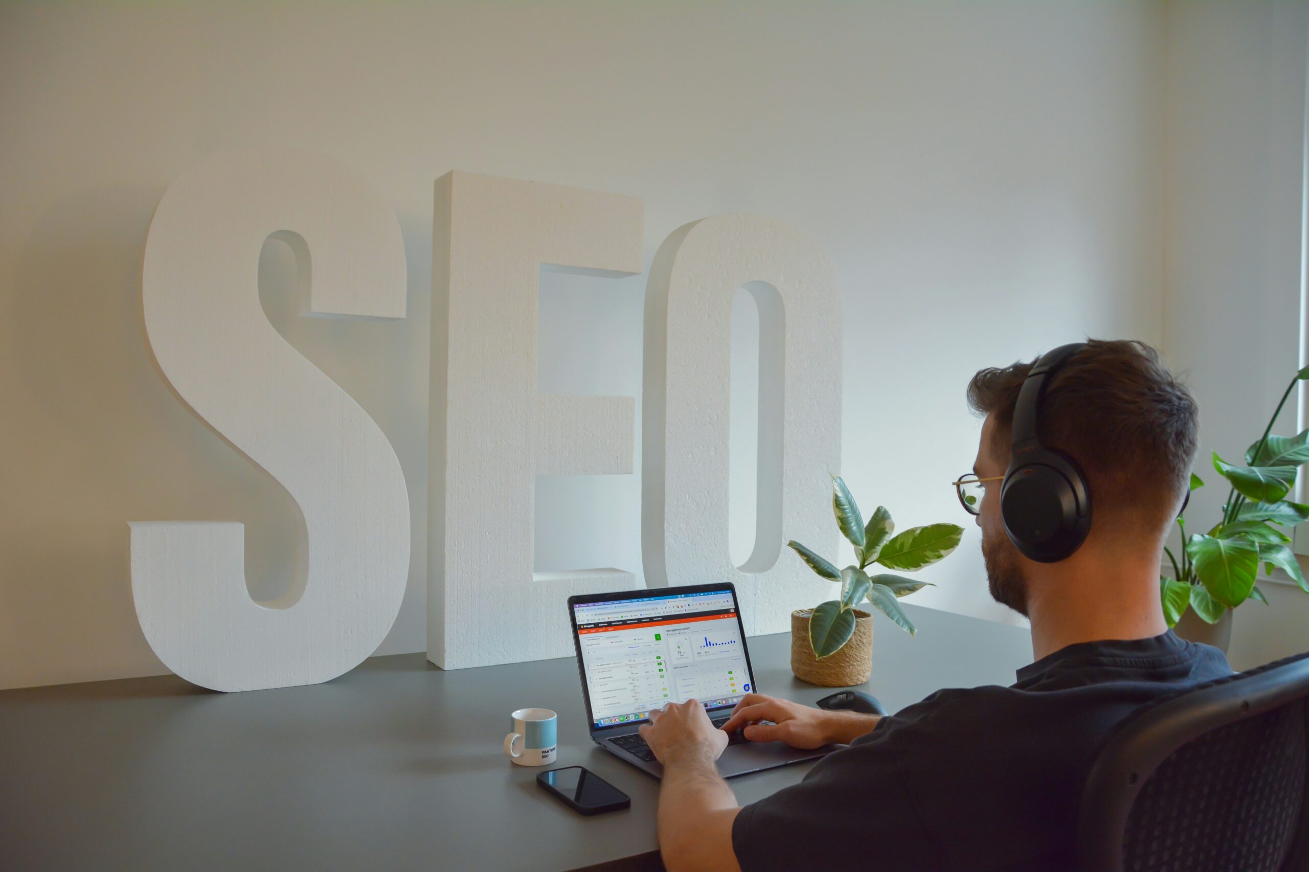 A digital marketer analyzing performance metrics on a laptop beside large SEO letters, representing the key elements behind successful SEO content marketing.