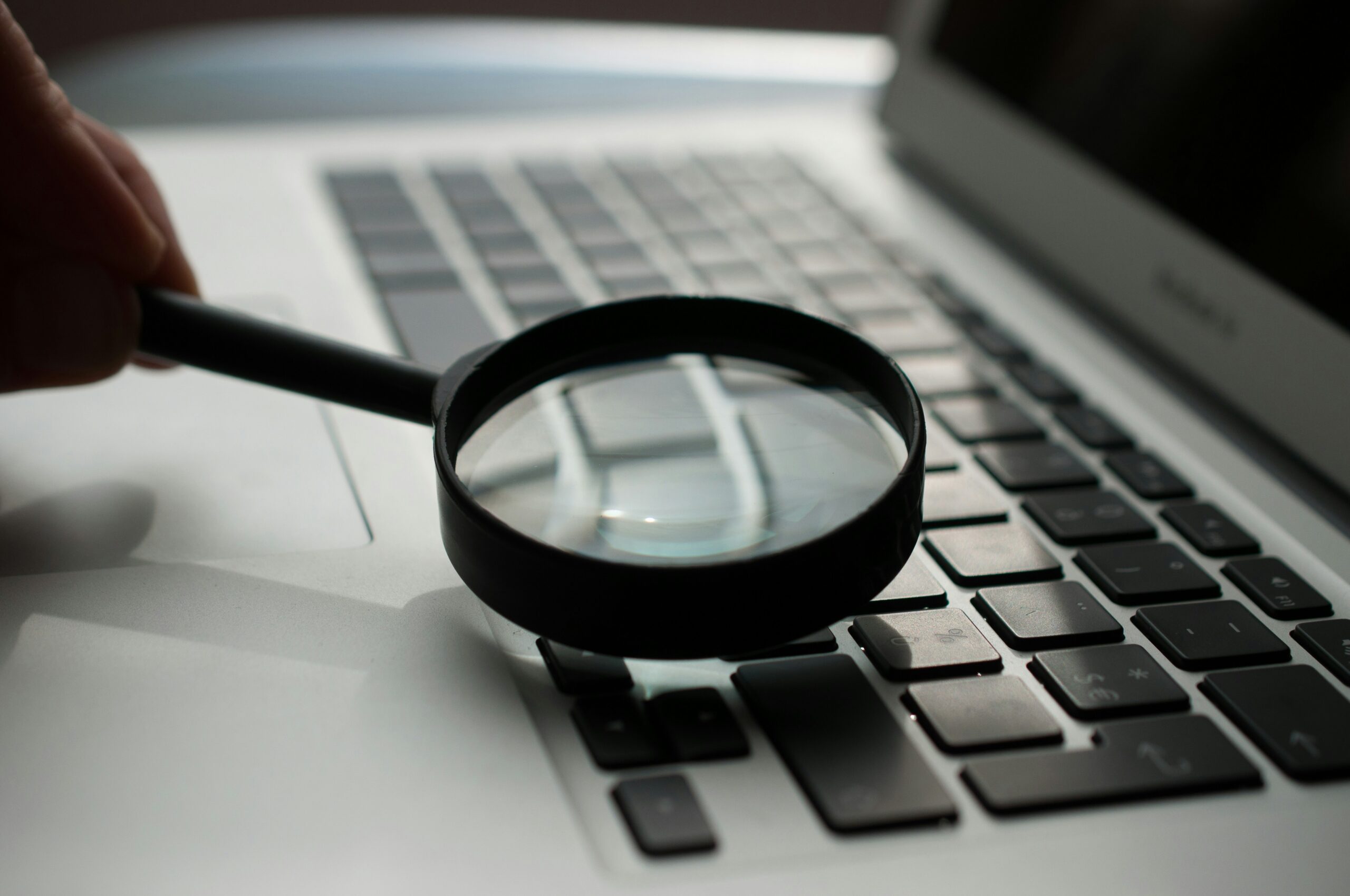 A magnifying glass held over a laptop keyboard, representing in-depth keyword research for SEO content. | Day by Day Digital A magnifying glass held over a laptop keyboard, representing in-depth keyword research for SEO content.