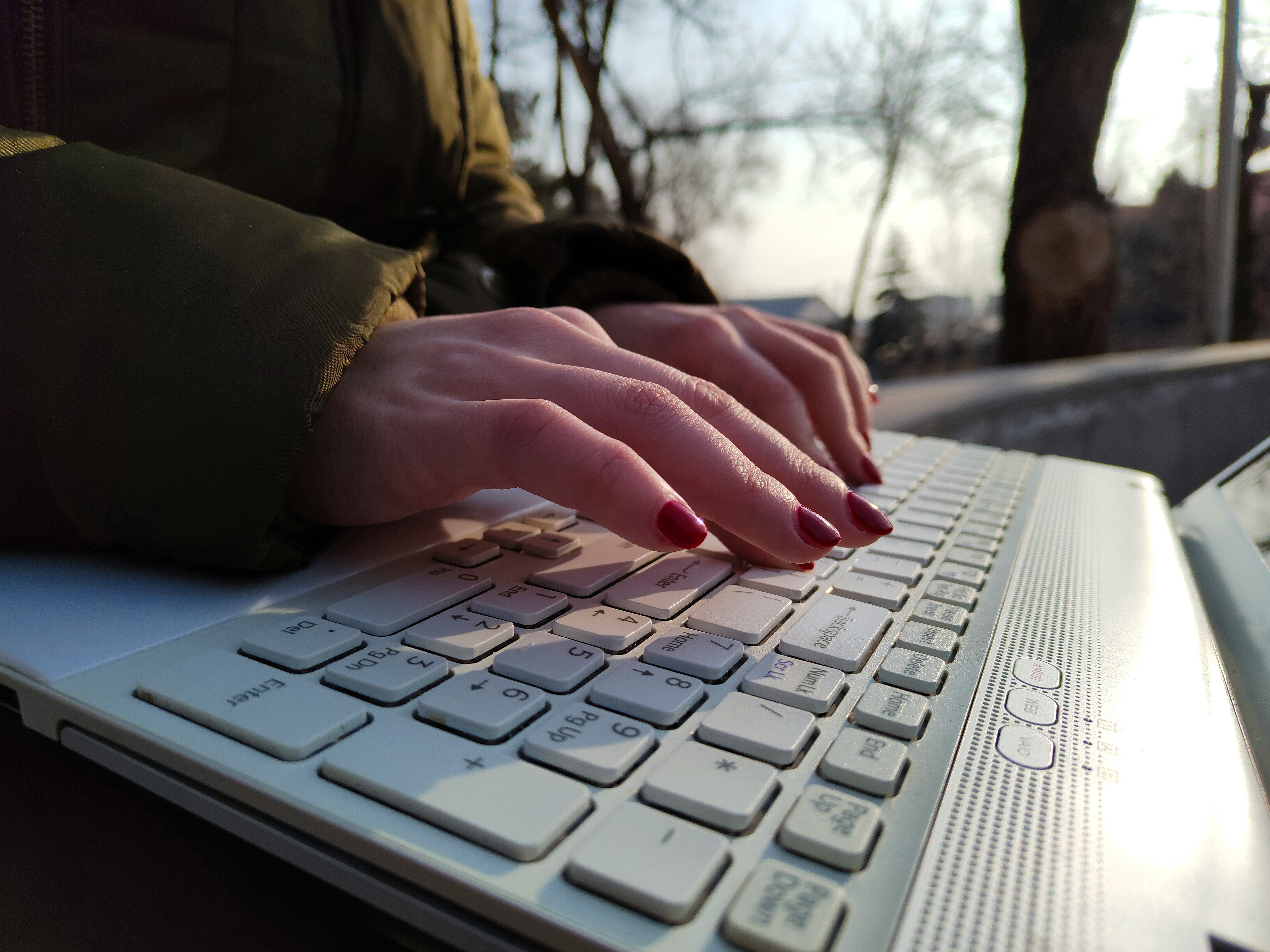 Close-up of hands typing on a laptop outdoors, representing the role of SEO content providers in crafting optimized digital content that boosts online visibility.