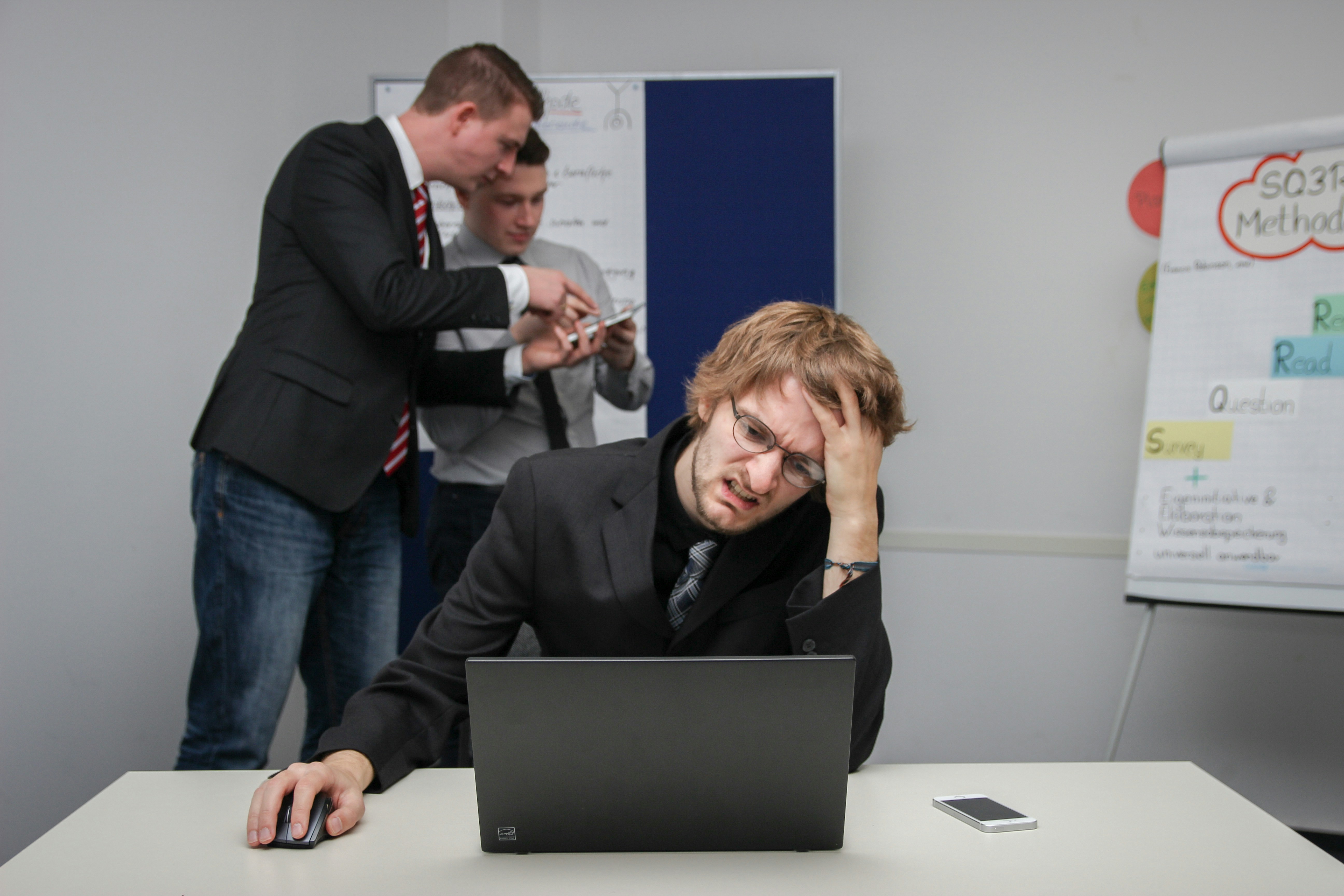 A frustrated man at a laptop with colleagues in the background, symbolizing common challenges businesses face in SEO content creation. | Day by Day Digital A frustrated man at a laptop with colleagues in the background, symbolizing common challenges businesses face in SEO content creation.